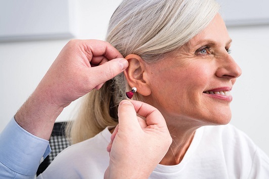 Ältere Frau bekommt ein modernes Hörgerät angepasst, Hörakustik und Hörhilfe Beratung.